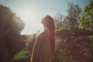 A woman is standing in a garden closing her eyes in the sun. The Leica R lens is pointed straight into the sun which creates a lens flare and takes away the contrast of this shot.