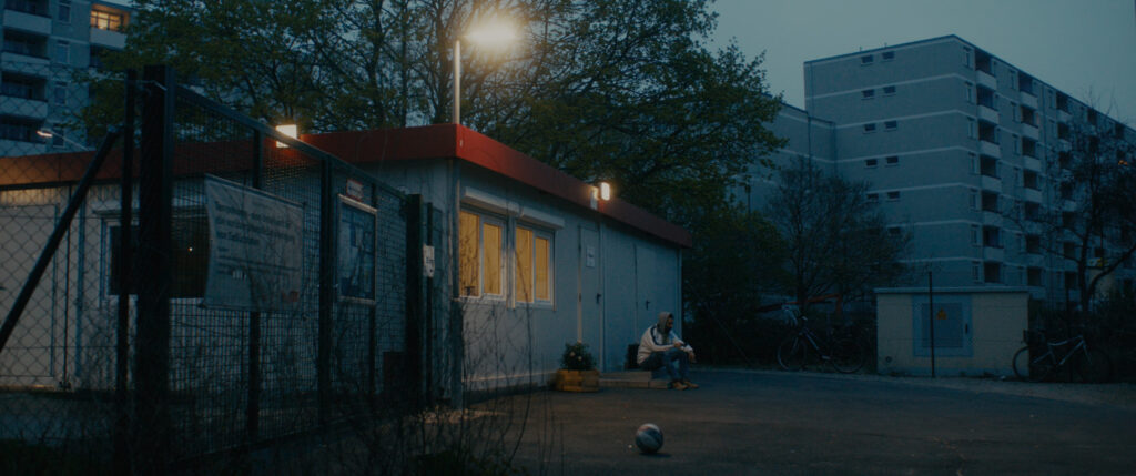 Blue hour. Man sitting in front of a container surrounded by blocks of flats. Shot on Super Speeds.