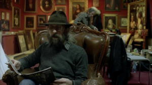 Two old bearded men are sitting in a small art gallery. One is reading a magazine. In the background you see copies of masterpieces of art history. Shot of Zeiss High Speed Super16 lenses.