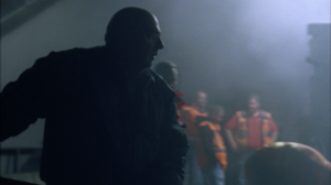 Silhouette shot of a road construction worker. A group of construction workers standing in the hazy background lit by a construction light from top.