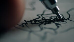 The tip of a ball pen is doodling on a grey piece of paper. Ultra close up shot.