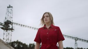 Medium low angle shot of a woman wearing a red polo shirt in front of a cloudy sky. Unsharp structures in the bokeh.