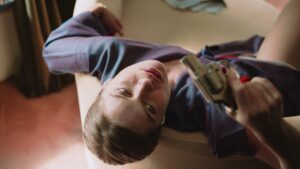 Top shot of a woman in a blue dress sitting on a couch holding a revolver. The depth of field is low due to the open aperture of the Leica R cinema lens.
