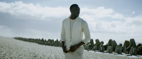 Young man in front of wave breakers standing on a beach. Cumulus clounds in the background. 
Short on LOMO Square Fronts.