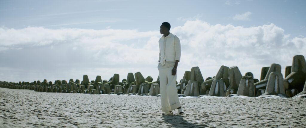 A male person in white clothes on a sand beach. Behind him there is a line breakwaves made from concrete.
Short on LOMO Square Fronts.