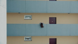 A wide shot of a woman letting her hair fall from the balcony. Blue and pale yellow colors making a strong palet. Captured with a Cooke Varotal Zoom.