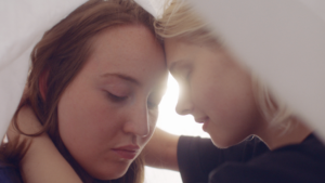 Close up shot of two women facing each other with theire eyes closed. The sun creates a lens flare. Shot with a Zeiss High Speed cinema lens.