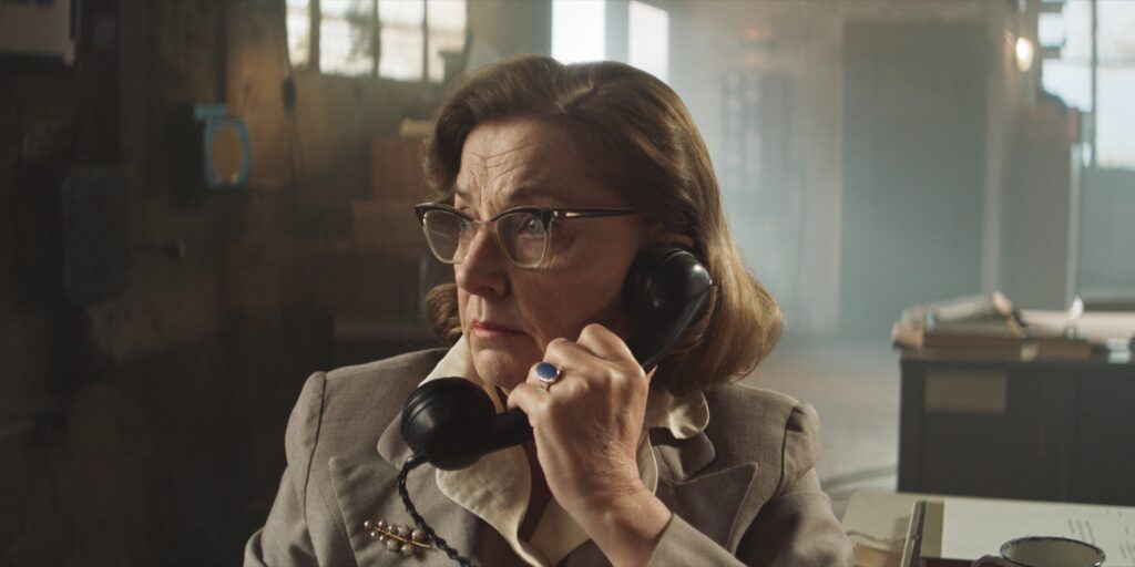 Medium close up shot of a woman holding a land line phone. The sun is visible due to the dusty background. The unsharp elements in the background show chromatic aberration typical for the Clavius cine primes.