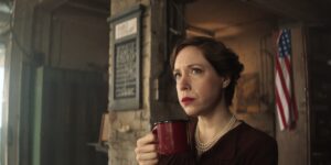 Wide angle medium close up of a woman in an old American building in front of an American flag is holding a cup. Shallow background with vintage bokeh.