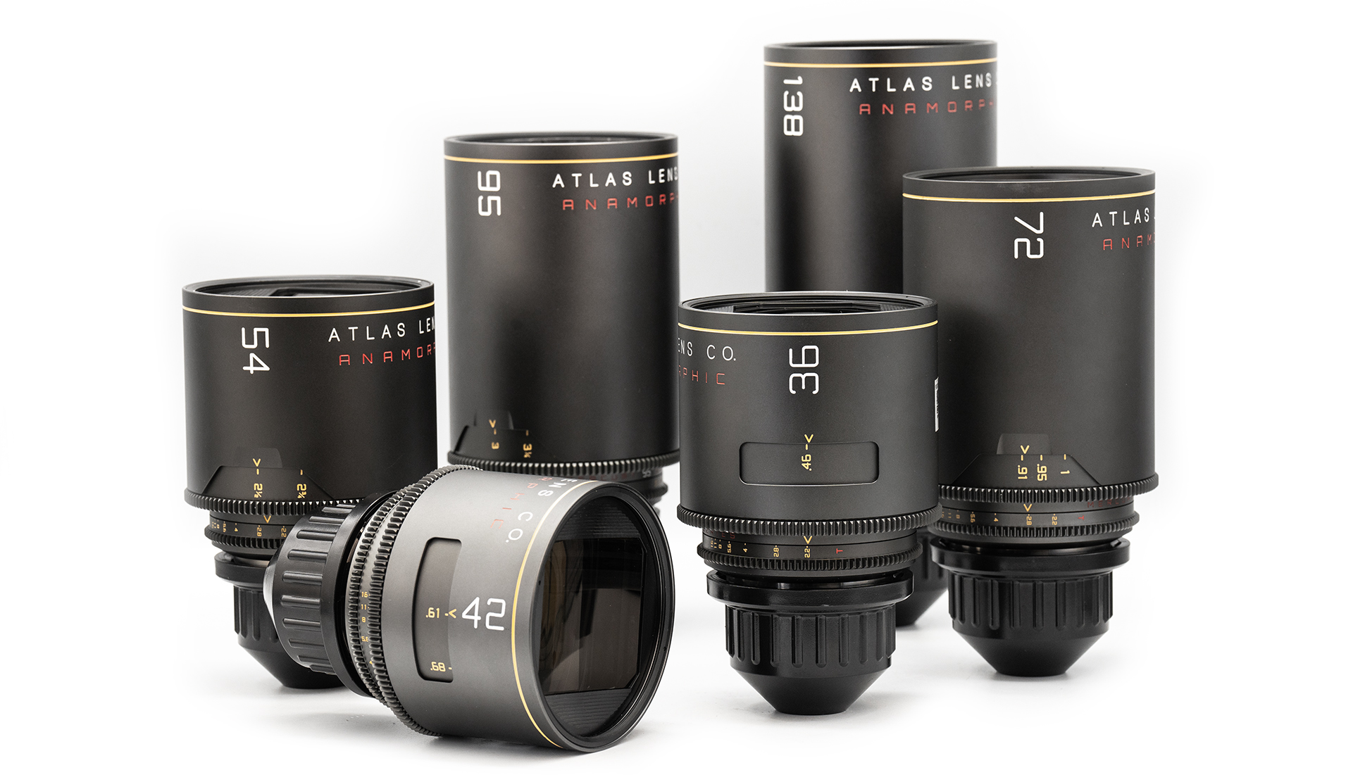 Six black Atlas anamorphic lenses of varying sizes are arranged together, standing upright, with one lens lying on its side. Each lens is labeled with its respective focal length, including 24mm, 36mm, 42mm, 54mm, 95mm, and 138mm. The lenses have a sleek, matte finish with gold and red accents on the markings.